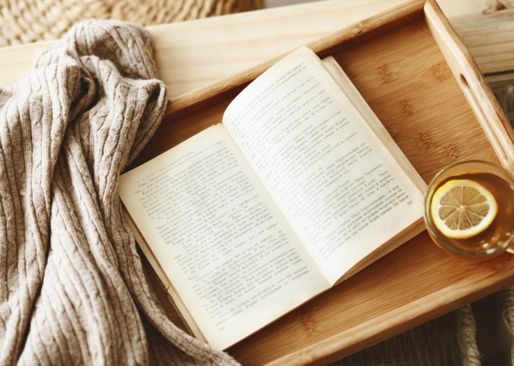 A book and sweater along with a beverage are kept on a brown surface.