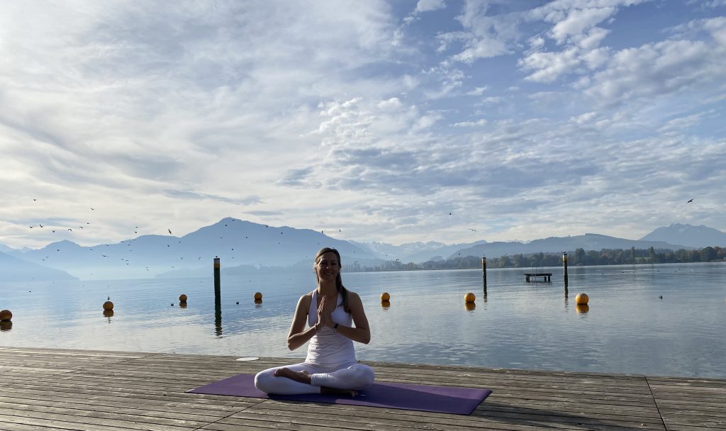 A woman smiling and meditating by a river body.