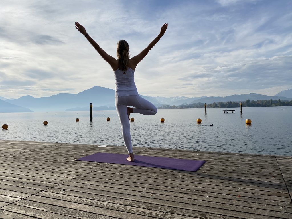 A woman doing Yoga by a large water body.