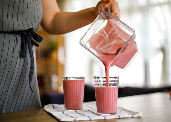 A woman pouring smoothie from a mixer into a glass.
